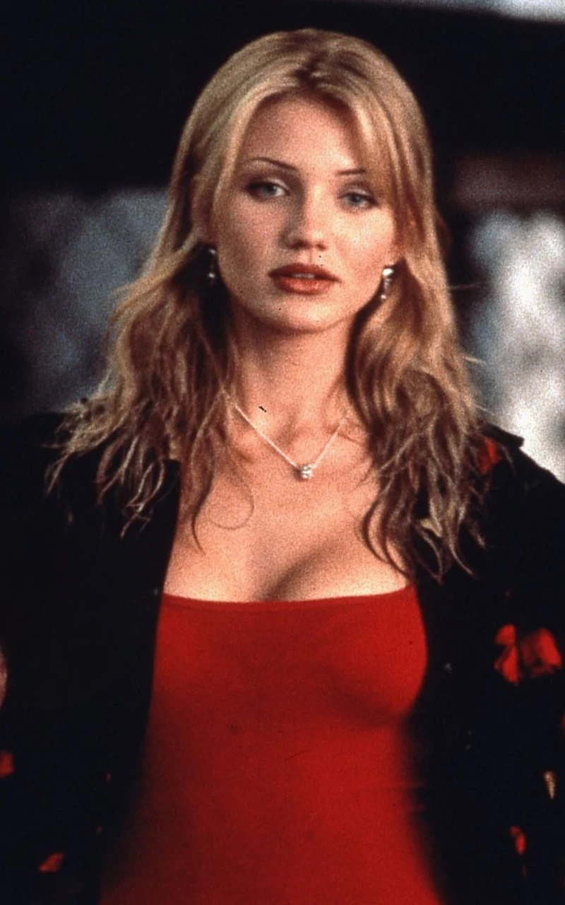 Kobieta o długich, blond włosach i delikatnym makijażu ubrana w czerwoną sukienkę oraz czarną narzutkę, nosząca srebrny naszyjnik, patrzy przed siebie z lekko poważnym wyrazem twarzy.