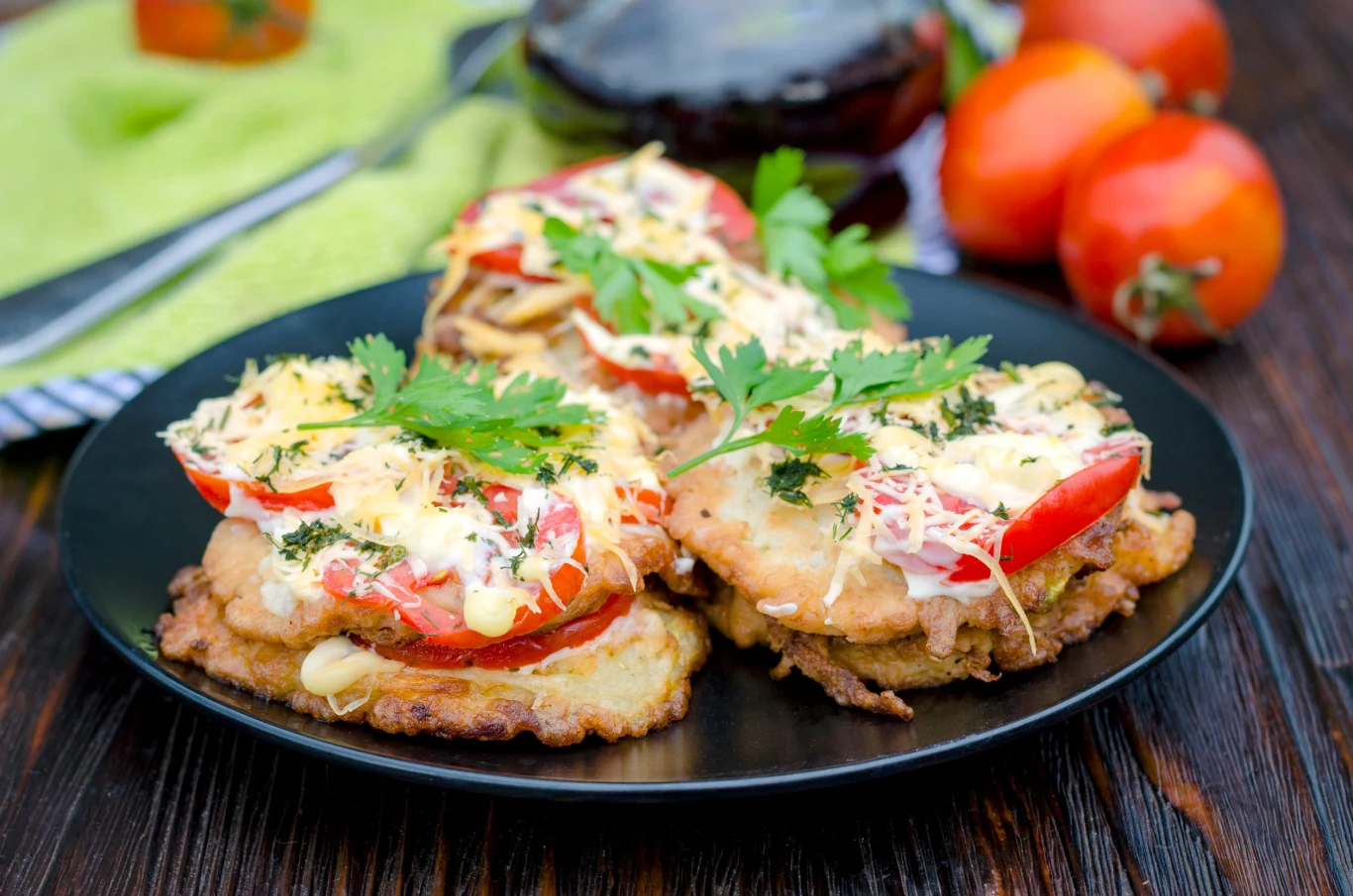 Zucchini appetizer. Zucchini pancakes with tomato sauce and grated hard cheese. Placki ziemniaczane z pomidorami, startym serem, kurczakiem i natką pietruszki na czarnym talerzu.