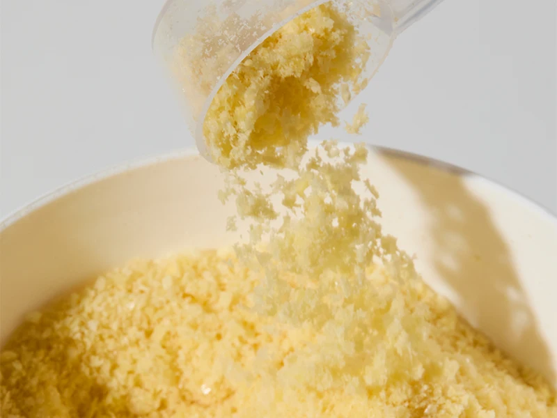 Colostrum w skutecznym budowaniu odporności Porcja żółtego proszku o drobnej, sypkiej konsystencji wsypywana z plastikowej miarki do jasnej miski.