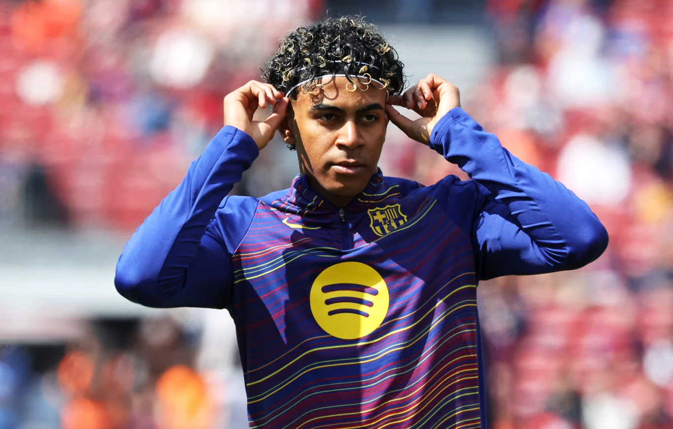 Młody piłkarz w rozgrzewkowej koszulce FC Barcelony z logotypem Spotify na piersi poprawia opaskę na głowie, stojąc na tle rozmytych trybun stadionu.