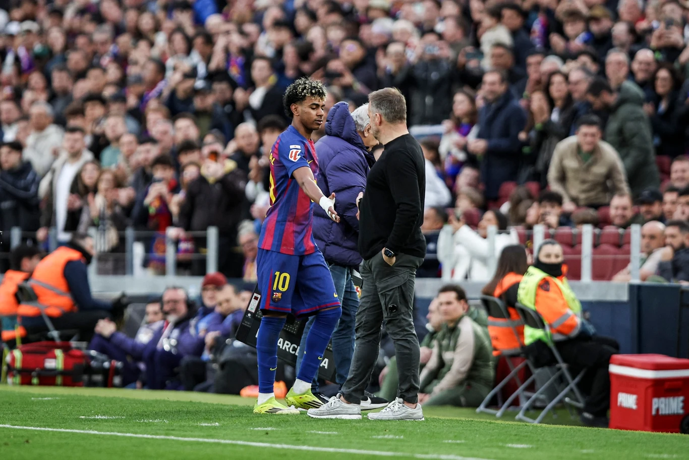 piłkarz w koszulce Barcelony z numerem 10 opuszcza boisko i podaje rękę trenerowi, w tle siedzący na ławce rezerwowych zawodnicy oraz kibice na trybunach