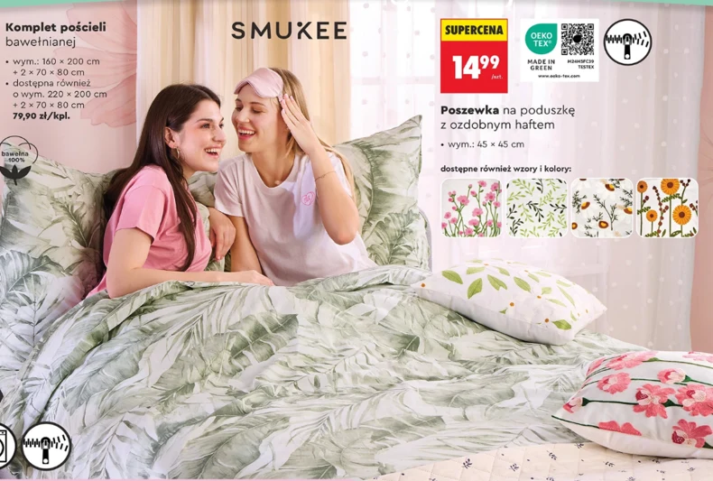 dwie młode kobiety w piżamach siedzące razem na łóżku z zieloną pościelą w liście, śmieją się i rozmawiają, wokół znajdują się ozdobne poduszki z roślinnymi wzorami oraz umieszczone oferty na pościel i poszewki z kwiatowymi motywami