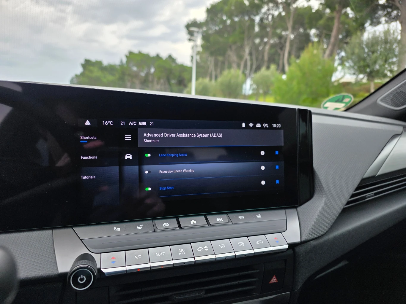 duży ekran multimedialny samochodu wyświetlający menu systemów wspomagania kierowcy, takich jak utrzymanie pasa ruchu, dynamiczne ograniczenie prędkości i asystent zatrzymania, otoczony nowoczesnym panelem sterowania z fizycznymi przyciskami i pokrętłe...