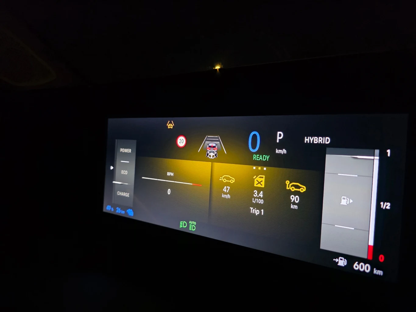 cyfrowy panel kokpitu samochodu hybrydowego z wyświetlonymi wskaźnikami prędkości, zasięgu elektrycznego i spalinowego, poziomu paliwa, informacjami o trybie jazdy oraz ostrzeżeniami o układzie bezpieczeństwa