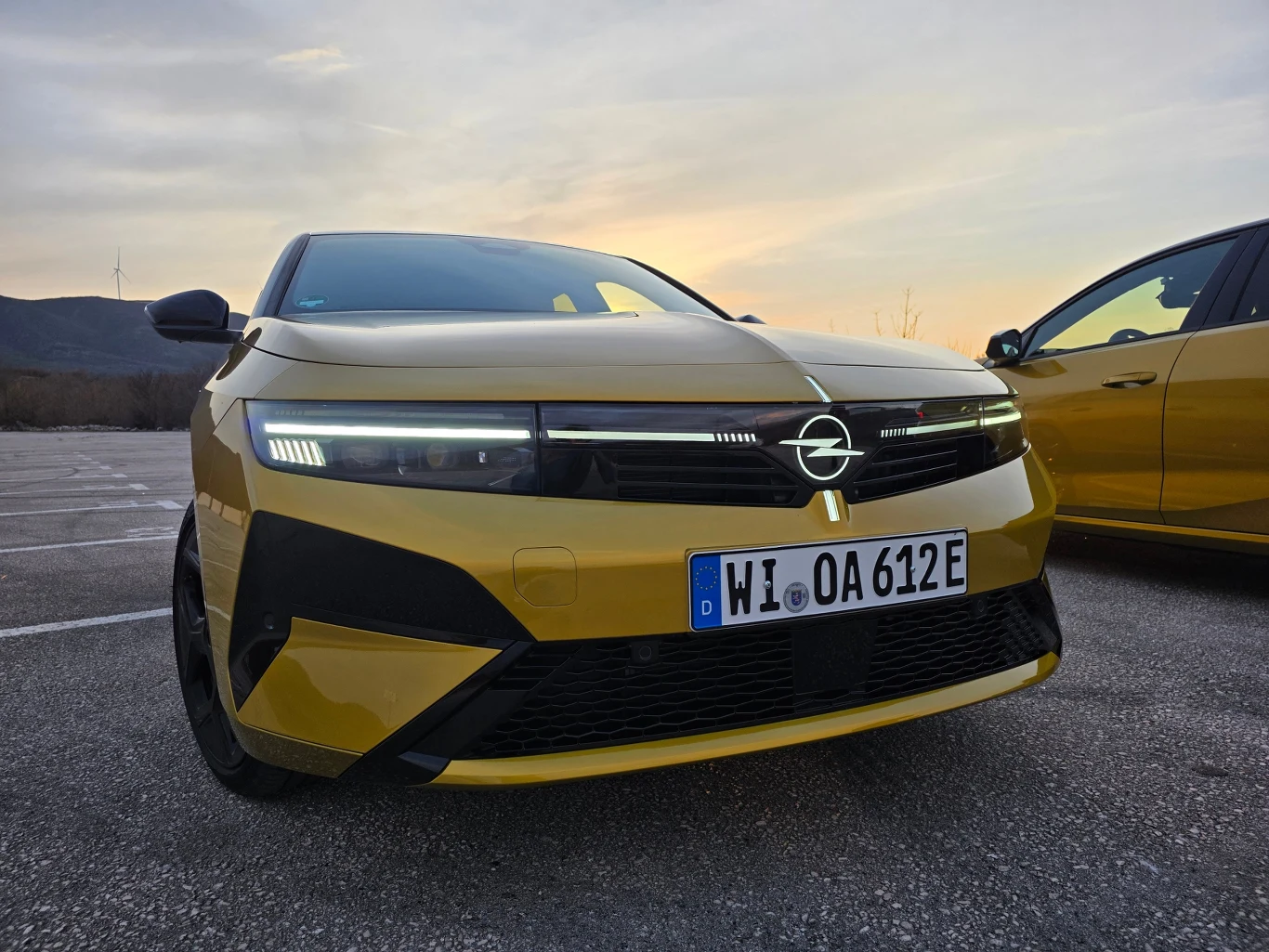 Nowoczesny, żółty Opel z charakterystycznym przednim grillem, światłami LED i niemiecką tablicą rejestracyjną, zaparkowany na otwartym parkingu przy zachodzącym słońcu.