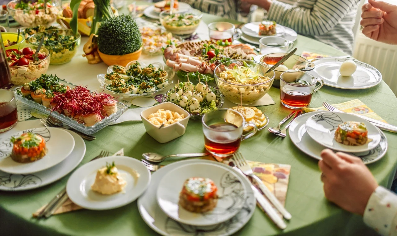 Polska Wielkanoc Wielkanocny stół z zielonym obrusem, dania i napoje, przy stole siedzą osoby gotowe do posiłku.