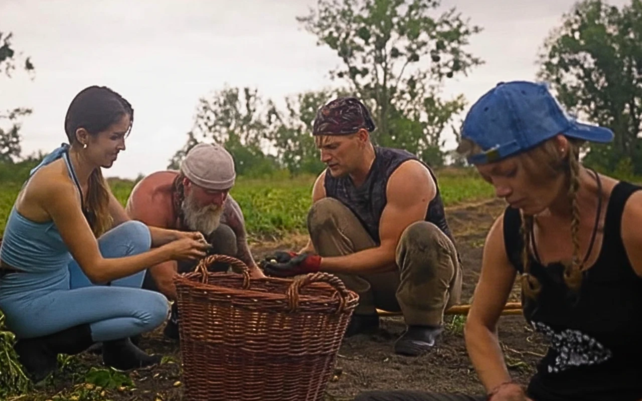"Farma" Uczestnicy programu „Farma” zbierają warzywa na polu i wkładają je do dużego wiklinowego kosza; w tle drzewa.