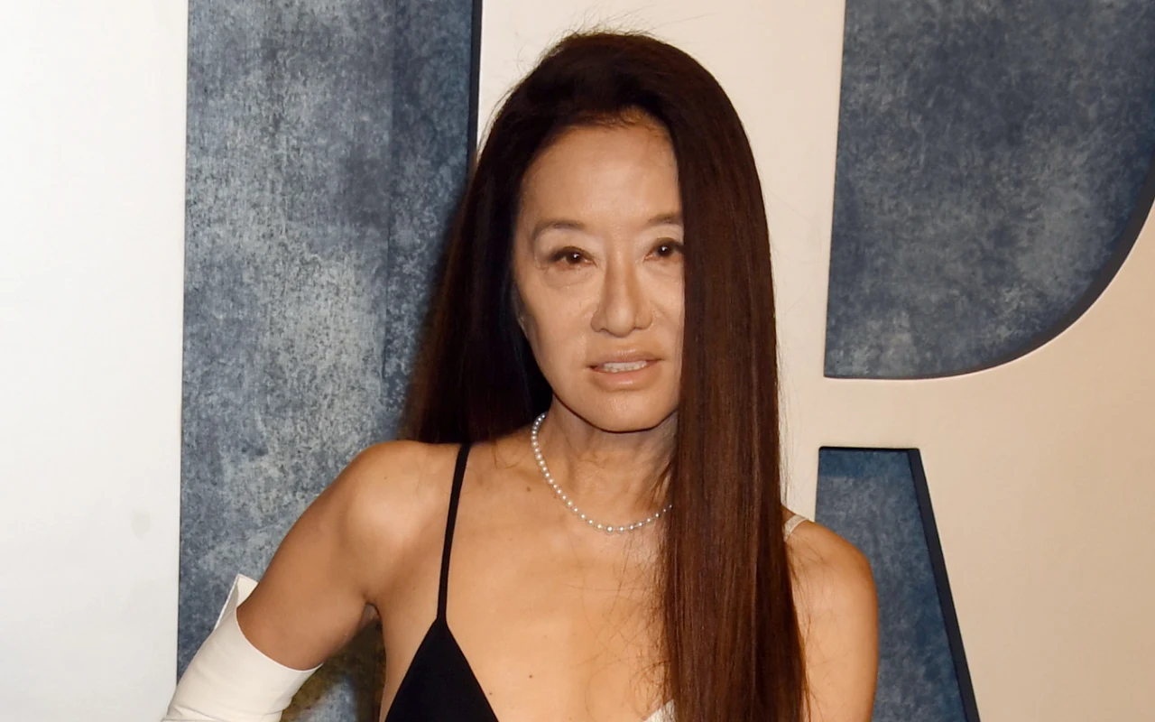 kobieta o długich, prostych włosach ubrana w czarną sukienkę z cienkim ramiączkiem i perłowym naszyjnikiem, stojąca na tle złożonym z białych i niebieskich elementów graficznych