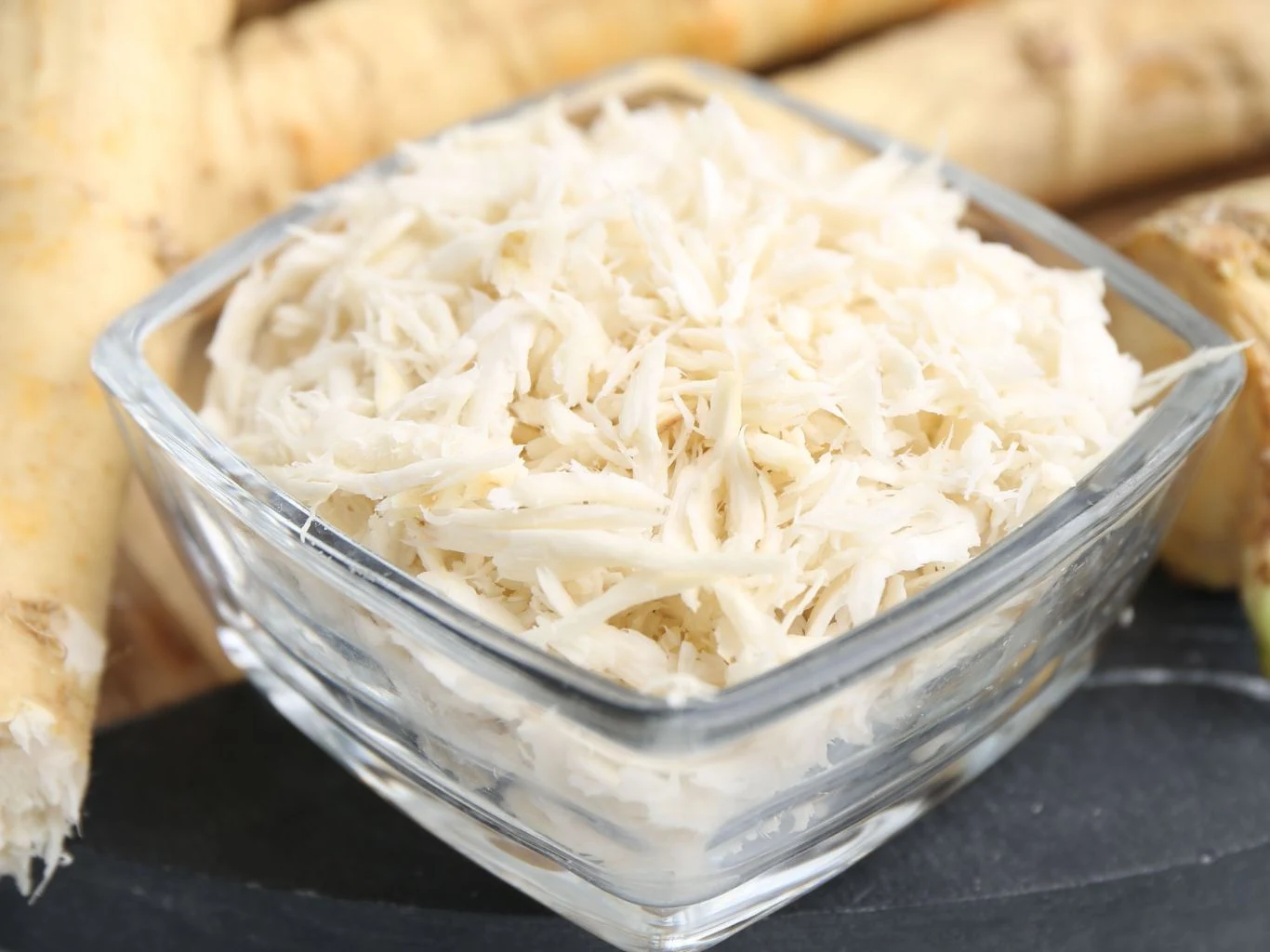 W polskich ogrodach go nie brakuje, a my jemy najczęściej raz w roku. Świeżo starty chrzan w przezroczystej szklanej miseczce, w tle korzenie chrzanu