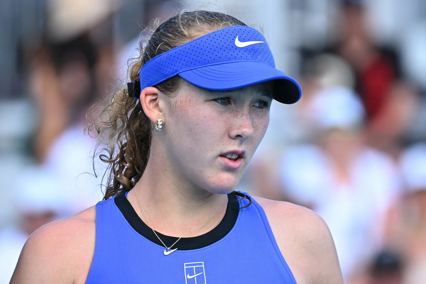 młoda kobieta w sportowym stroju i niebieskiej czapce z daszkiem, z zaciętą miną, na tle rozmytego tłumu