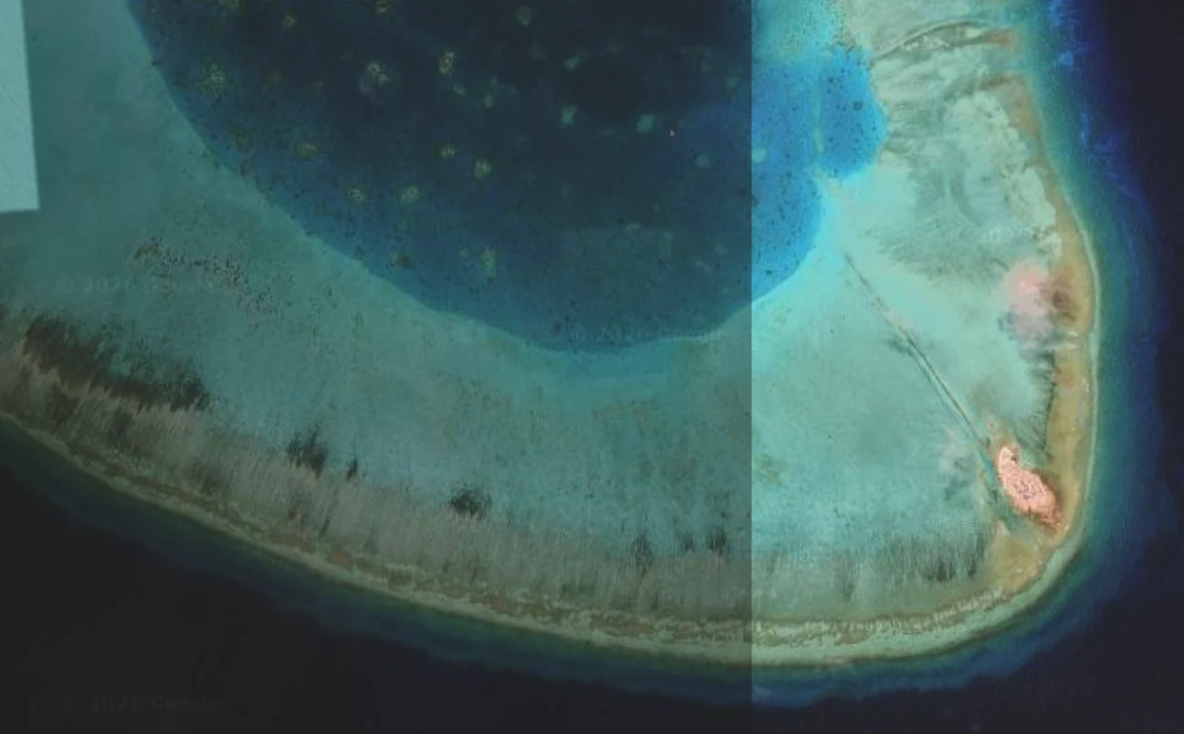 półksiężycowaty atol koralowy otoczony błękitną wodą, z wyraźnym jasnym obszarem lądu i pomarańczowymi fragmentami na jego końcu oraz kontrastującą ciemniejszą linią rafy