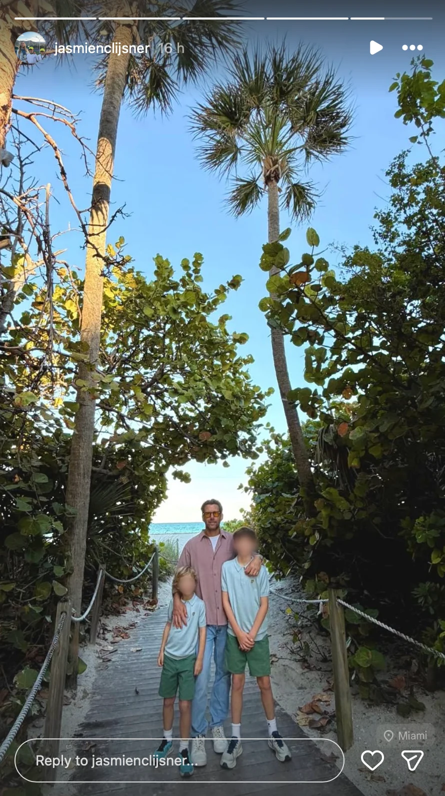 mężczyzna stoi z dwójką dzieci na drewnianej ścieżce prowadzącej przez zarośla do plaży, w tle widoczne palmy i fragment morza