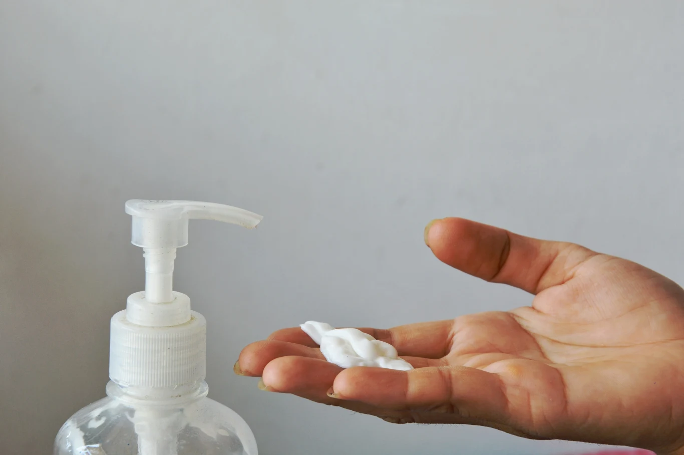 ręka z nałożoną porcją piany lub mydła w płynie, obok przezroczysta butelka z dozownikiem