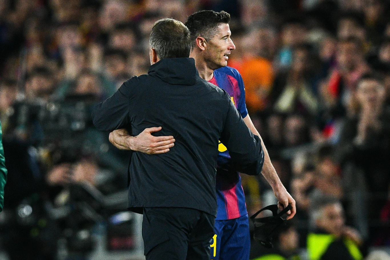Piłkarz w stroju FC Barcelony obejmuje trenera na murawie stadionu, wokół zgromadzeni kibice i fotografowie dokumentujący wydarzenie.