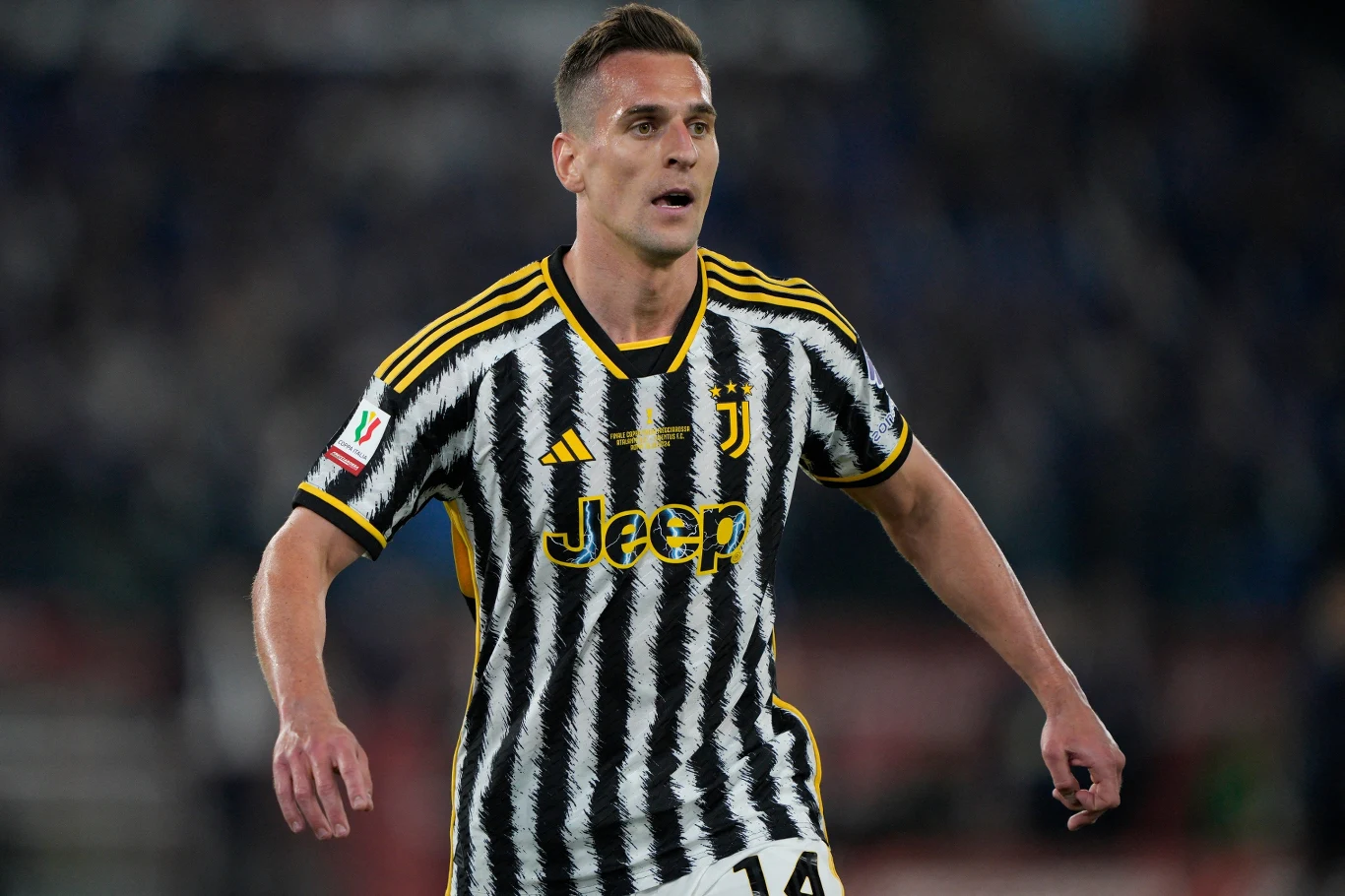 Arkadiusz Milik piłkarz w czarno-białej koszulce z żółtymi akcentami i numerem 14 na spodenkach reprezentuje Juventus podczas meczu, z logo Jeep na środku koszulki
