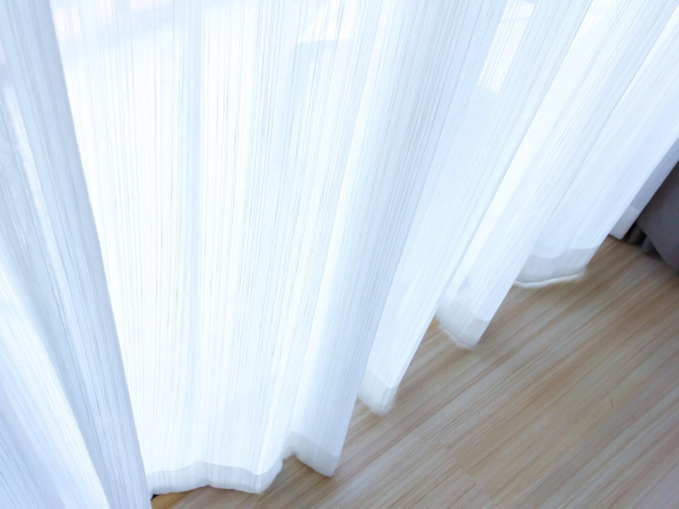 Przywróć swoim firankom biel na wiosnę Delikatne, białe firany przepuszczające światło, opadające na jasną, drewnianą podłogę