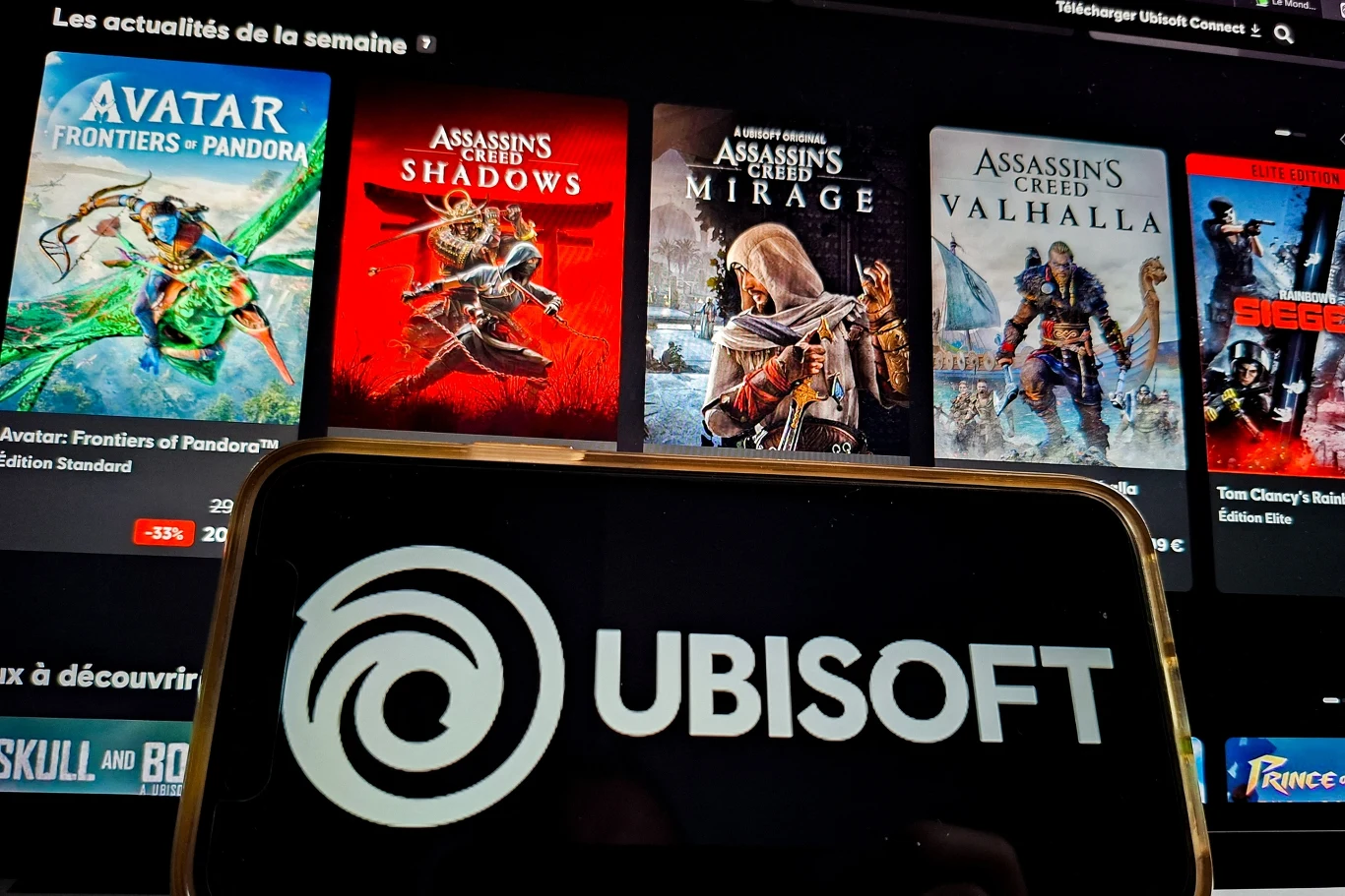 ekran z widocznymi okładkami najnowszych gier Ubisoft, takich jak Avatar: Frontiers of Pandora, Assassin’s Creed Shadows, Assassin’s Creed Mirage oraz Assassin’s Creed Valhalla, na pierwszym planie wyświetlone duże logo Ubisoft na ekranie smartfona