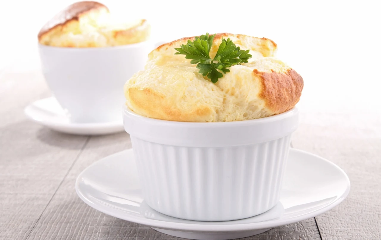 Suflet, czyli klasyka francuskiej kuchni Suflet serowy w białej kokilce, posypany natką pietruszki, podany na białym talerzyku na drewnianym stole.