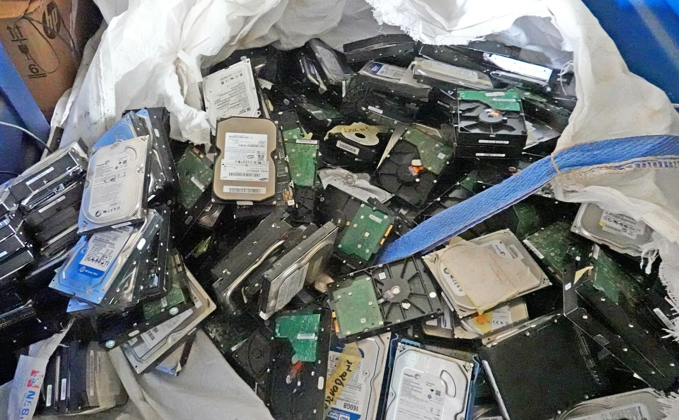 duża ilość używanych i uszkodzonych dysków twardych luzem wrzuconych do białego worka, z widocznymi odsłoniętymi podzespołami elektronicznymi
