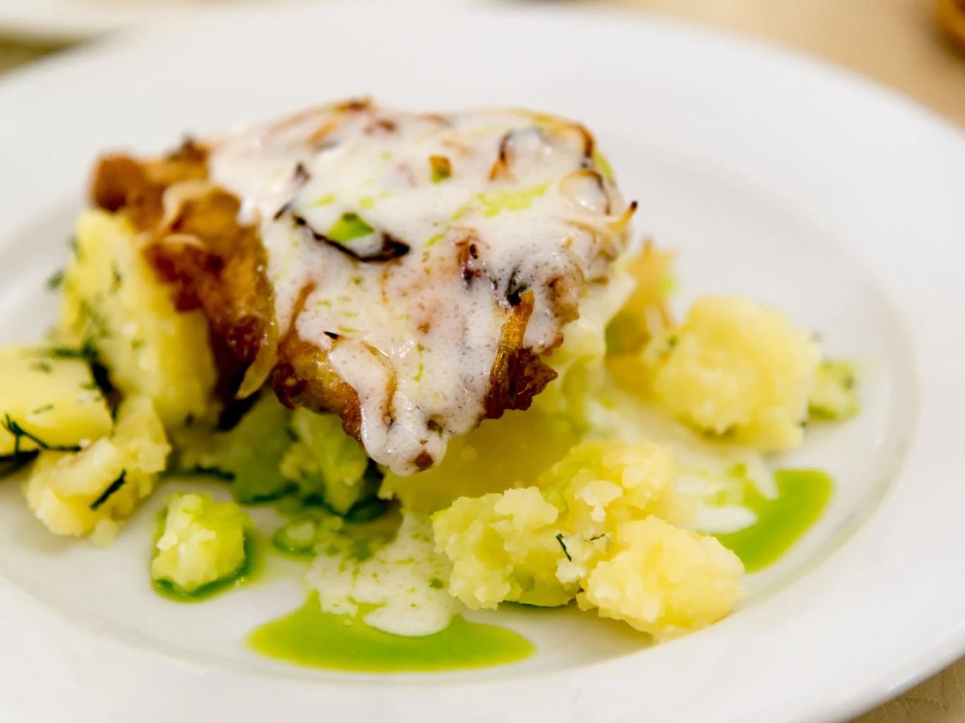 Ten dorsz z sosem czosnkowym świetnie pasuje na piątkowy obiad. Dorsz w sosie czosnkowym z plasterkami warzyw na puree ziemniaczanym i zielonym sosem, podany na białym talerzu