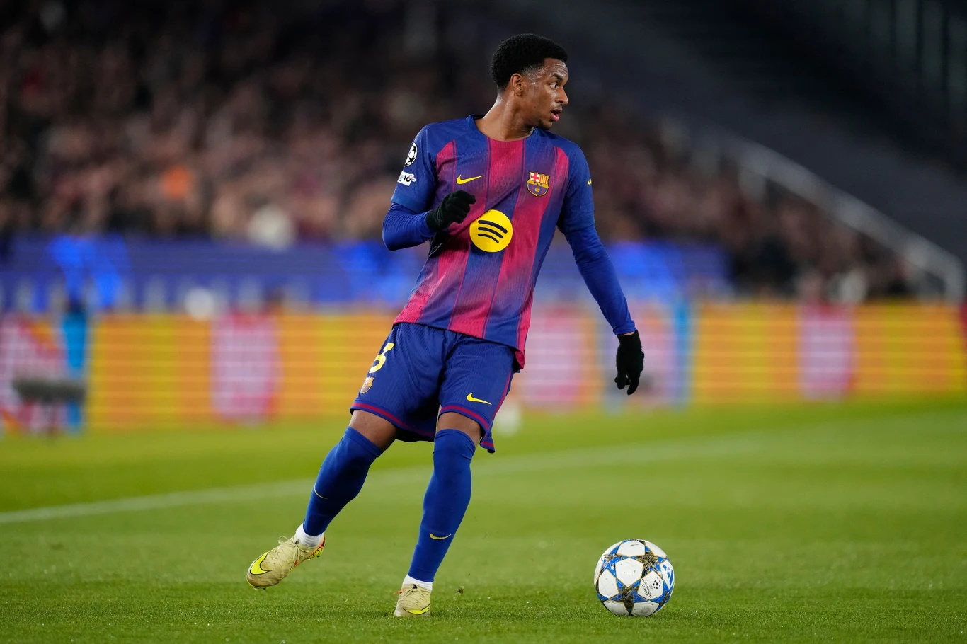 piłkarz w stroju FC Barcelony prowadzi piłkę po murawie podczas meczu, w tle rozmyta publiczność na stadionie