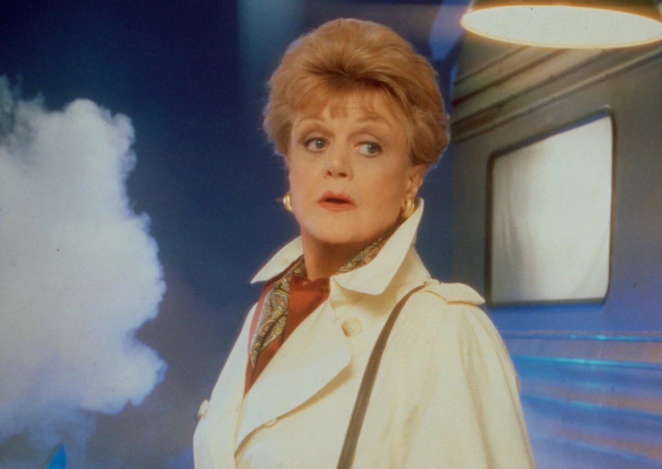 Kobieta w jasnym płaszczu z apaszką na szyi stoi na tle wagonu pociągu oraz wydobywającej się z boku pary; spogląda w bok z wyrazem powagi i skupienia na twarzy.