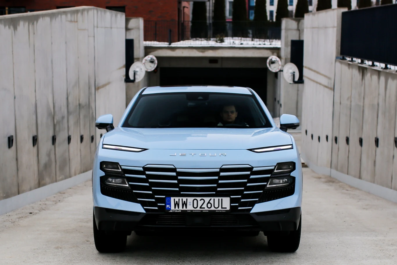 jasnoniebieski samochód marki Hyundai stoi przodem na zjeździe do podziemnego garażu, za kierownicą siedzi kierowca, w tle betonowe ściany wjazdu