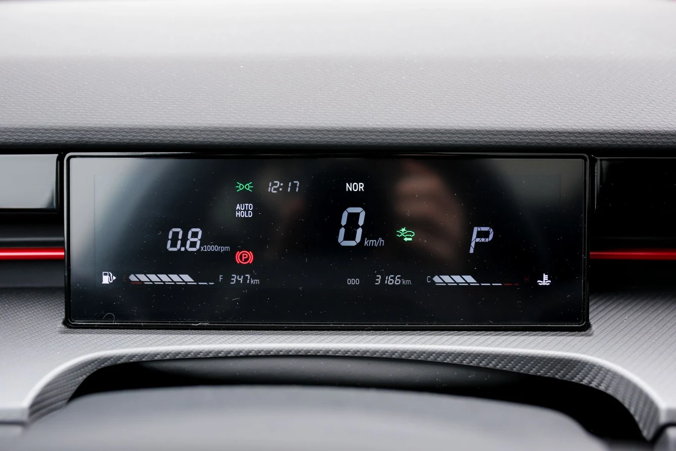 cyfrowy wyświetlacz samochodu prezentujący aktualną prędkość 0 km/h, tryb jazdy NOR, wskaźnik obrotów silnika, poziom paliwa, wskaźnik zasięgu, aktualny czas oraz wybór trybu PARK