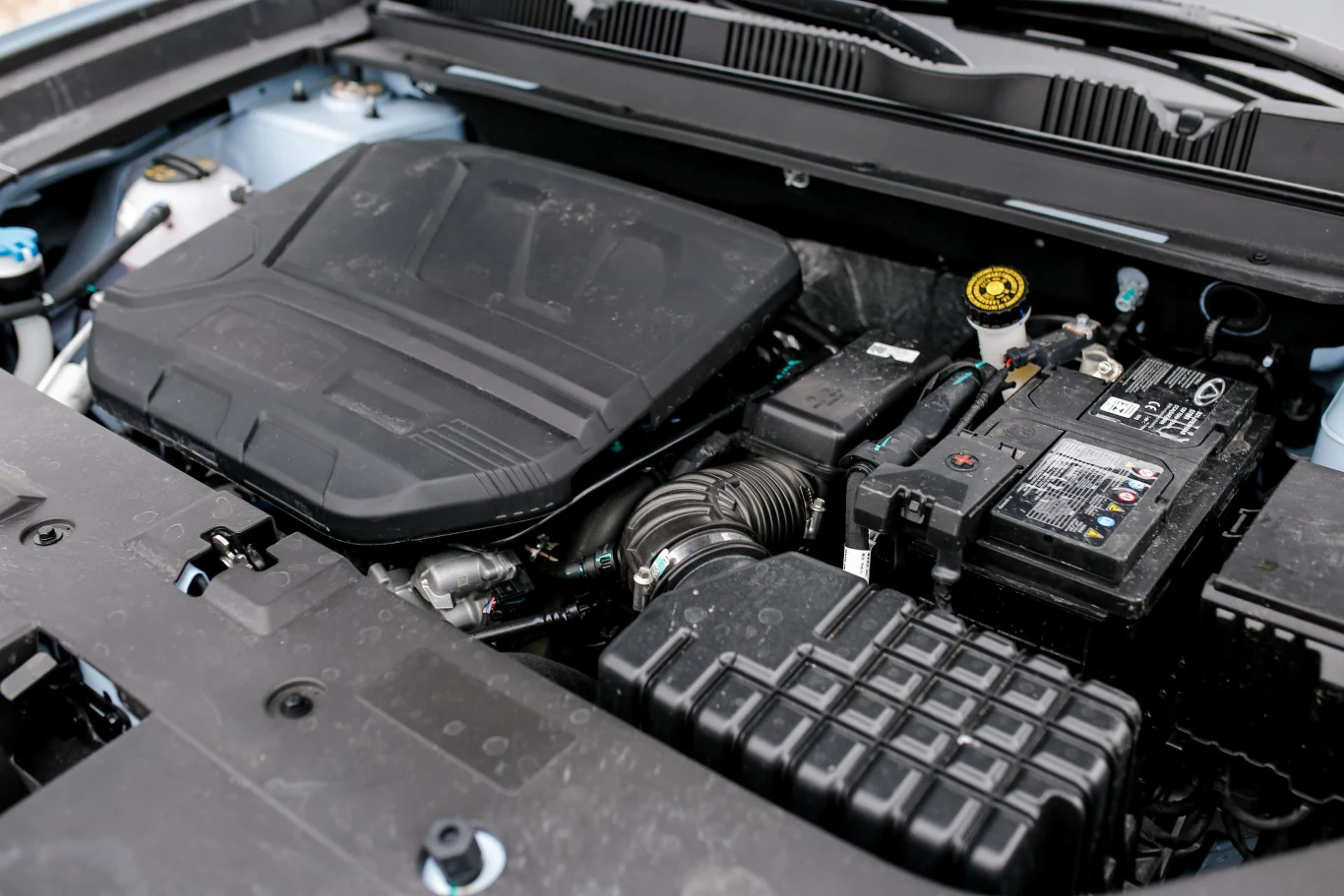 komora silnika samochodu z widoczną pokrywą silnika, akumulatorem, przewodami i plastikowymi obudowami elementów mechanicznych