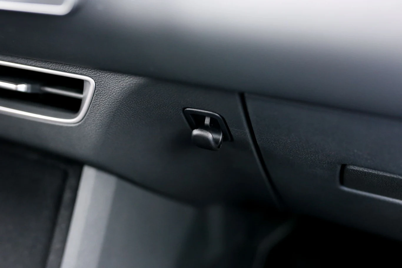 kokpit samochodu z widocznym schowkiem oraz kratką wentylacyjną po lewej stronie, na pierwszym planie uchwyt pozwalający otworzyć schowek pasażera