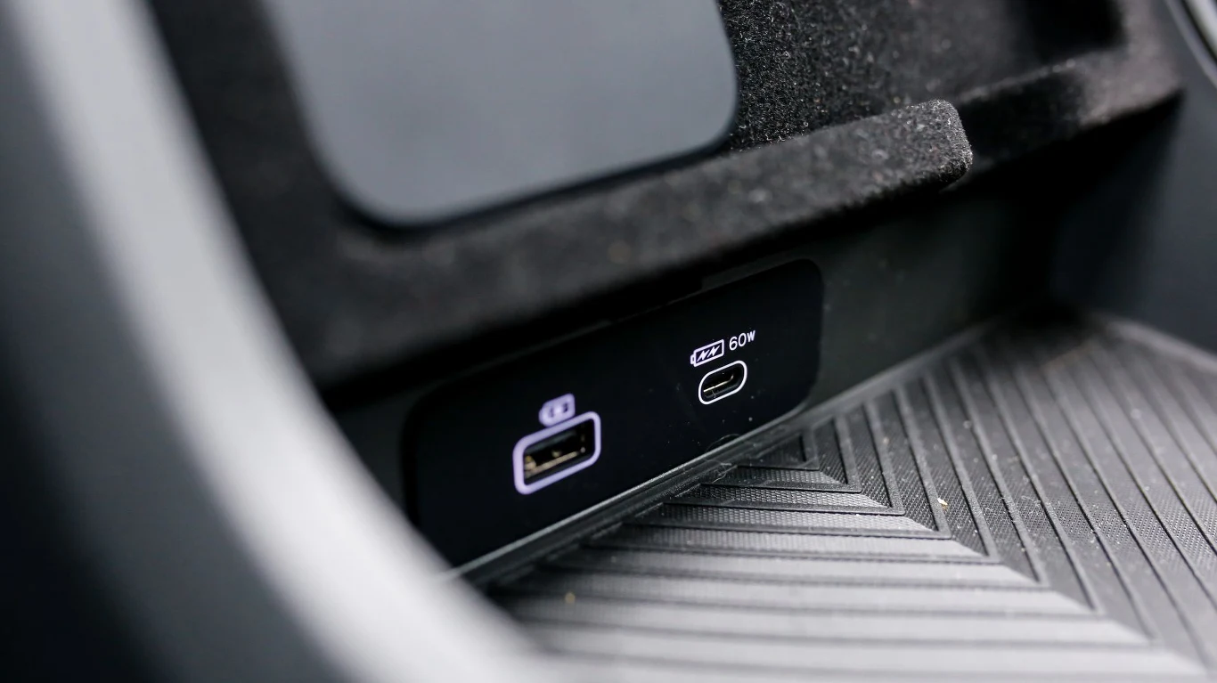 dwa porty ładowania w samochodzie, jeden USB-A i jeden USB-C oznaczony jako 60W, umieszczone w podłokietniku na tle żebrowanej, gumowanej powierzchni