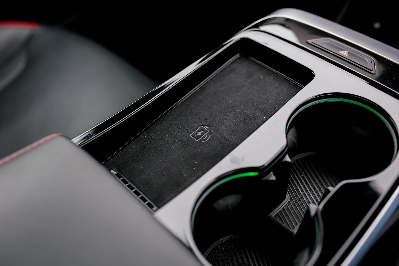 konsola środkowa samochodu z dwoma uchwytami na kubki, schowkiem wyposażonym w ładowarkę indukcyjną oraz widocznym przyciskiem awaryjnych świateł