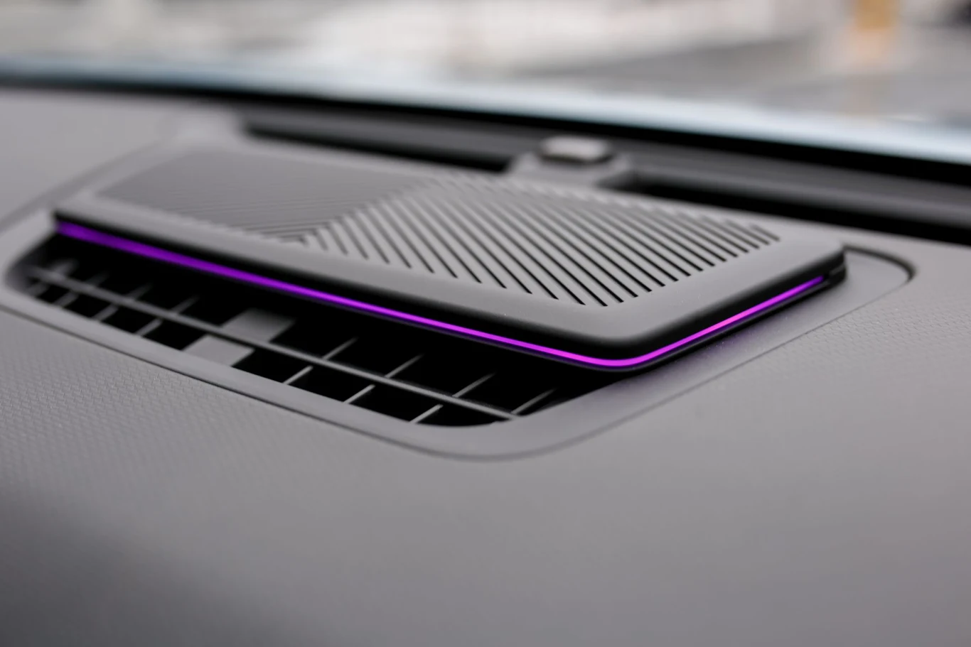 czarna, prostokątna kratka wentylacyjna wewnątrz samochodu z nowoczesnym panelem ozdobionym fioletowym podświetleniem, znajdująca się na górze deski rozdzielczej