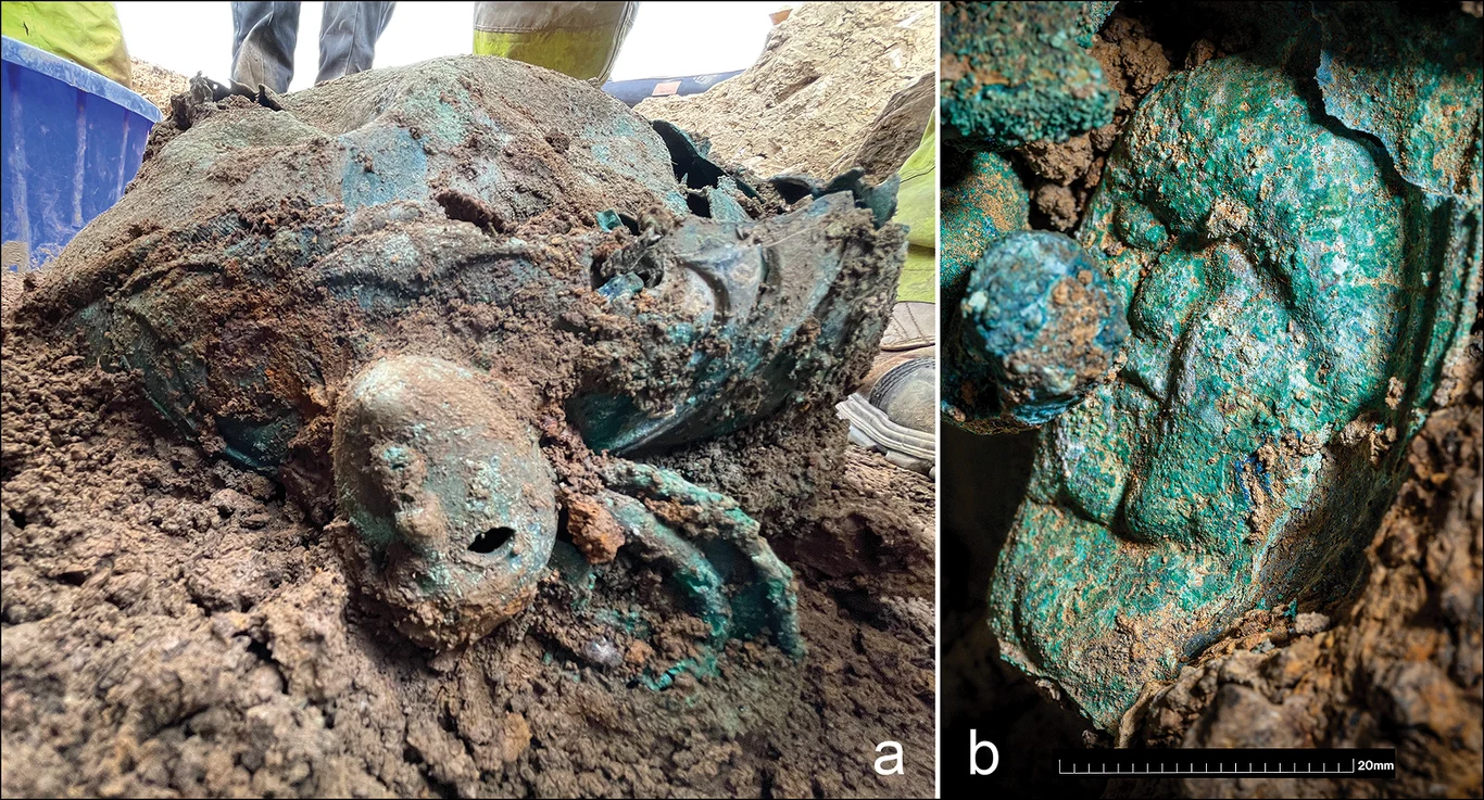 Znalezisko archeologiczne w postaci dużej, metalowej głowy pokrytej patyną, częściowo zakopanej w ziemi, z wyraźnymi detalami twarzy i widocznymi uszkodzeniami na powierzchni oraz zbliżenie na szczegóły rzeźby pokazujące teksturę i korozję metalu.