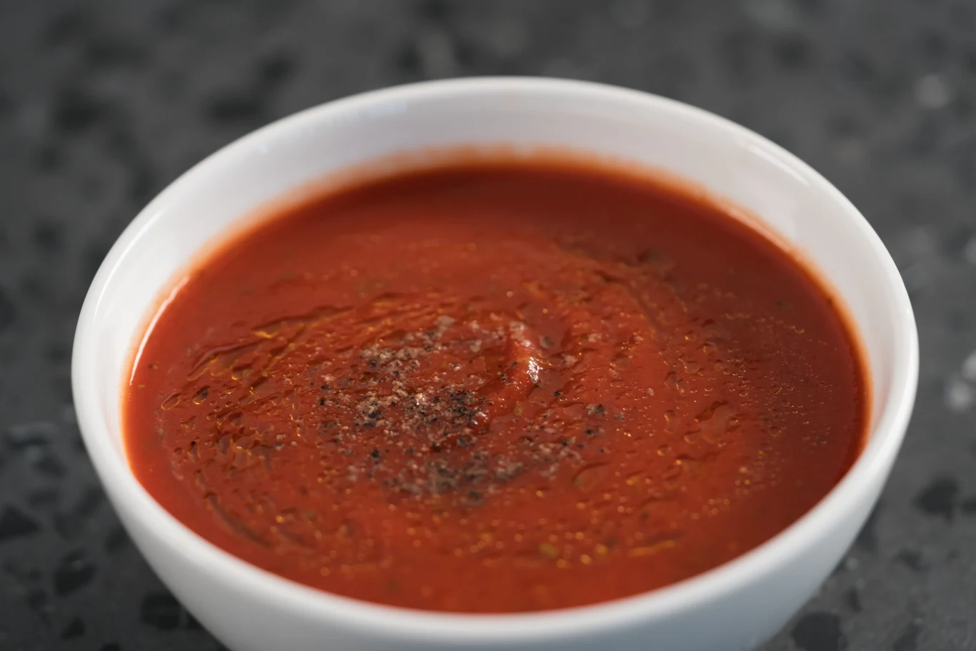 gęsty sos pomidorowy podany w białej miseczce, z delikatnie oprószoną powierzchnią świeżo zmielonym czarnym pieprzem