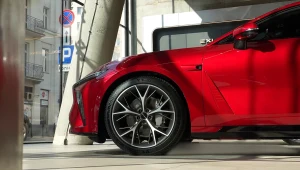 czerwony samochód sportowy zaparkowany w salonie, z dużymi aluminiowymi felgami i nowoczesnym wzornictwem nadwozia, promienie słońca odbijające się od karoserii