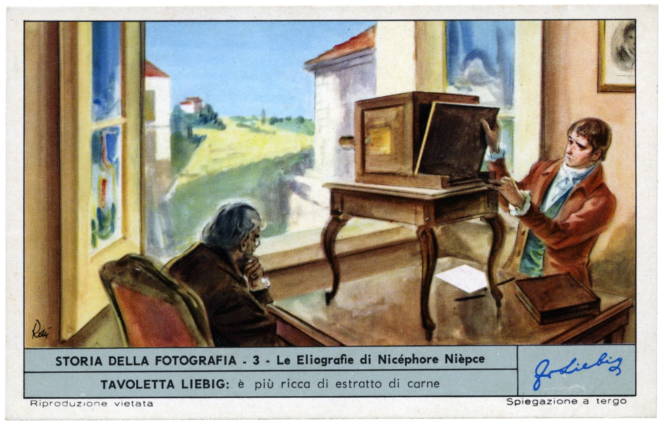 dwóch mężczyzn w pomieszczeniu, jeden siedzi przy stole z notatkami, drugi obsługuje duży aparat fotograficzny typu camera obscura ustawiony na ozdobnym stole, przez okno widać zielony krajobraz i fragment budynku