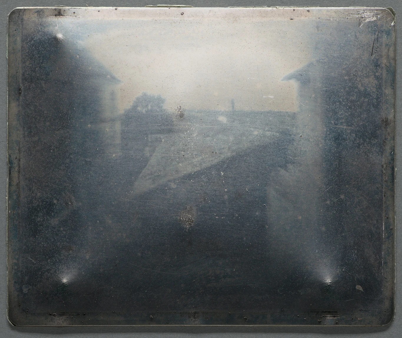 widok na podwórze otoczone dwoma budynkami z rozmytym, zamglonym tłem oraz zarysami drzew i odległego horyzontu