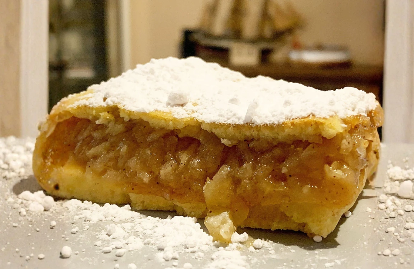 Do musu do szarlotki warto dodać nieco mąki ziemniaczanej, która wchłonie nadmiar wody Kawałek szarlotki z widoczną warstwą prażonych jabłek, kruchym spodem i cukrem pudrem na wierzchu.