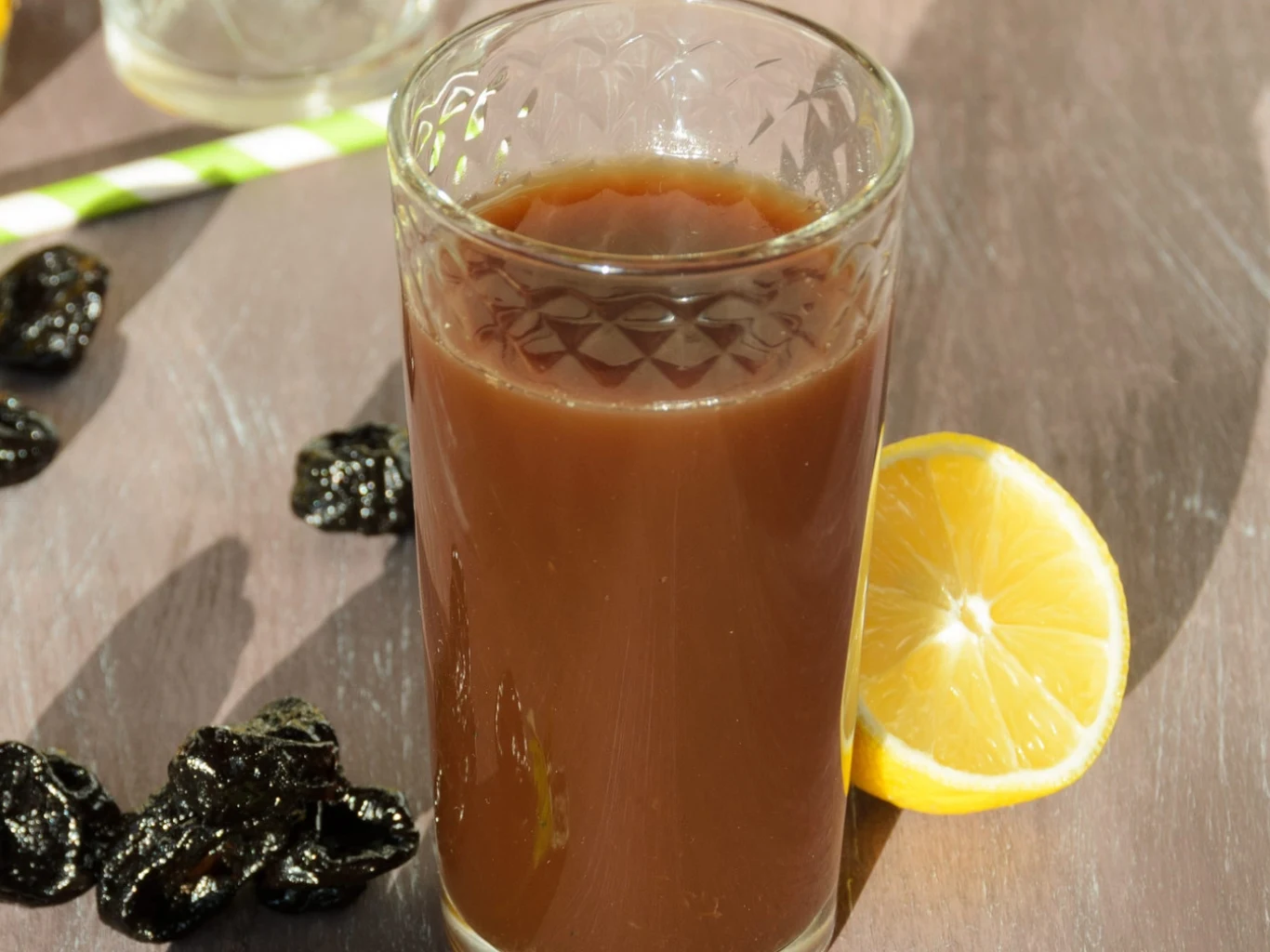 Sok z suszonych śliwek pobudza pracę jelit i dobrze działa na kości. Szklanka soku z suszonych śliwek na stole, napój wspierający jelita i zdrowie kości.