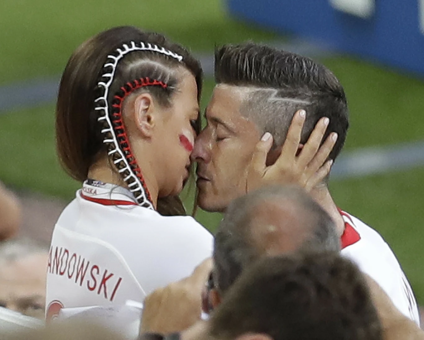 para ubrana w biało-czerwone stroje sportowe w emocjonalnym uścisku, kobieta z ciekawie zaplecionym warkoczem i czerwonym malowaniem na policzku dotyka twarzy mężczyzny, na tle stadionu