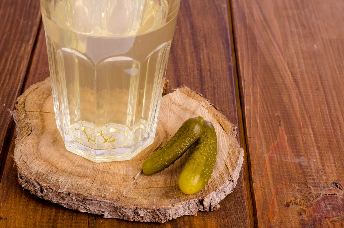 Dlaczego warto pić wodę po ogórkach? Sok z ogórków kiszonych w szklance, obok ogórki kiszone.