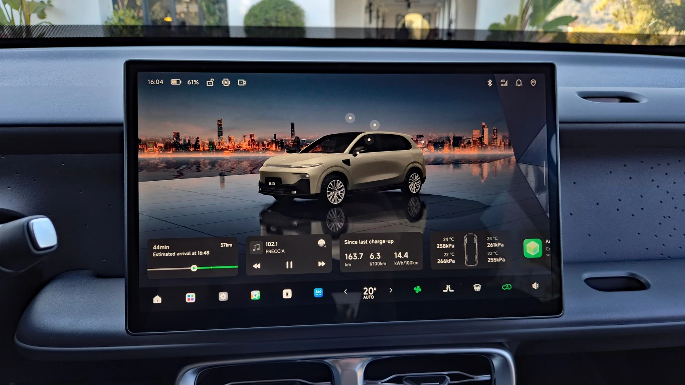 duży ekran dotykowy we wnętrzu samochodu wyświetlający wizualizację pojazdu elektrycznego, informacje o stanie naładowania akumulatora, szacowanym zasięgu oraz parametrach jazdy na tle panoramicznego widoku miasta