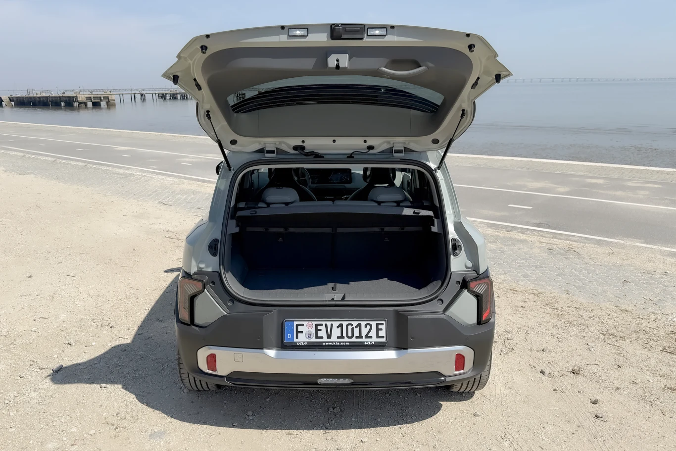 otwarty bagażnik nowoczesnego SUV-a elektrycznego zaparkowanego przy pustej, nadmorskiej drodze, z widoczną plażą oraz spokojnym morzem w tle