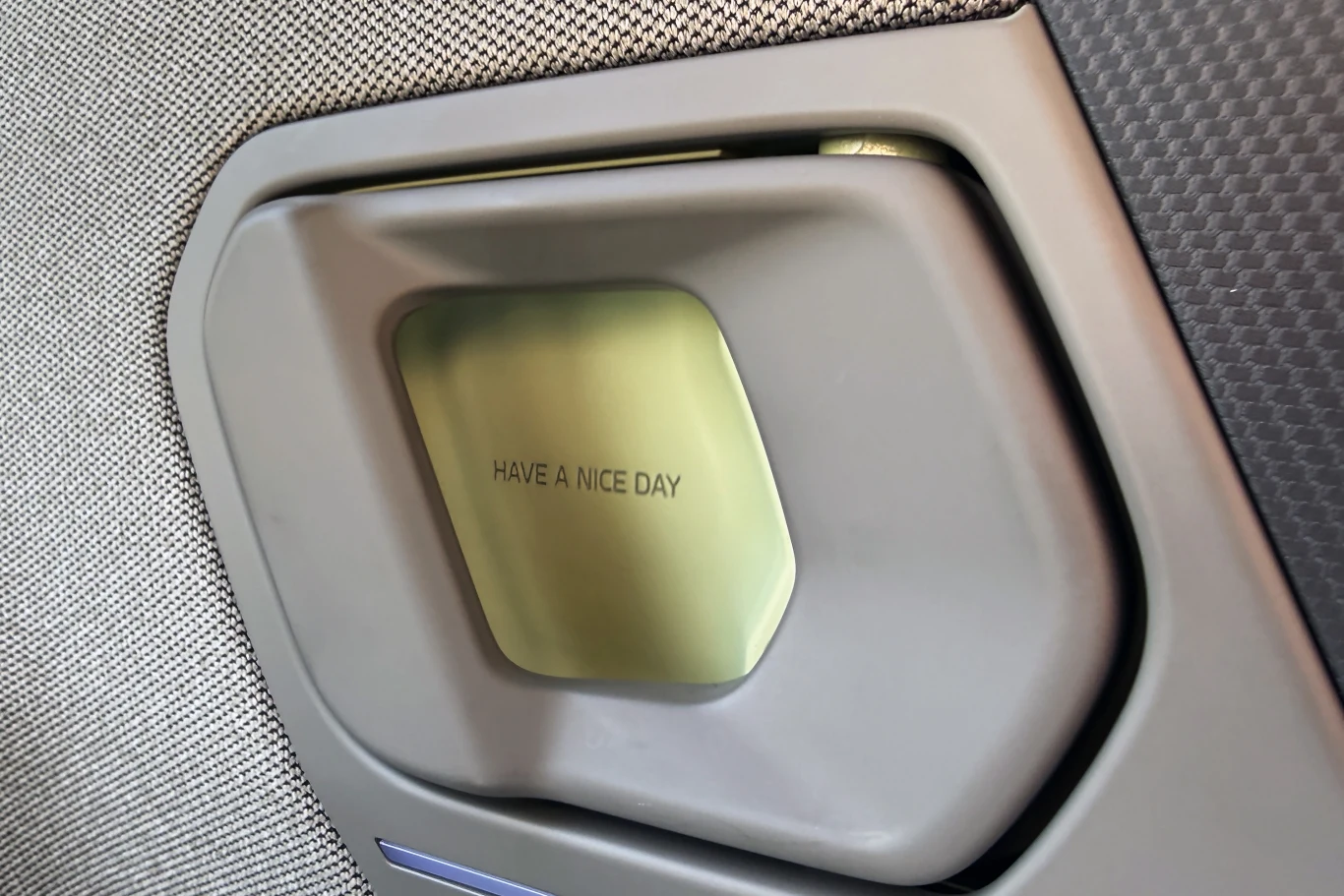 detal panelu z napisem „HAVE A NICE DAY” wytłoczonym na metalowej płytce, otoczonej szarą ramką, w tle widoczna faktura materiału tapicerskiego