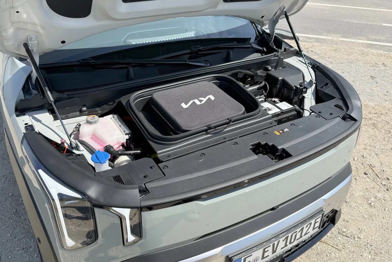 przedni bagażnik elektrycznego samochodu marki Kia z widocznym logo na pokrywie schowka, po lewej stronie zbiornik na płyn chłodniczy i elementy instalacji elektrycznej