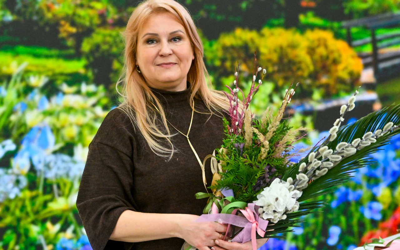 Anna Rządca Uśmiechnięta Anna Rządca trzyma w rękach bukiet zrobionych przez siebie palm świątecznych z baziami i kwiatami.