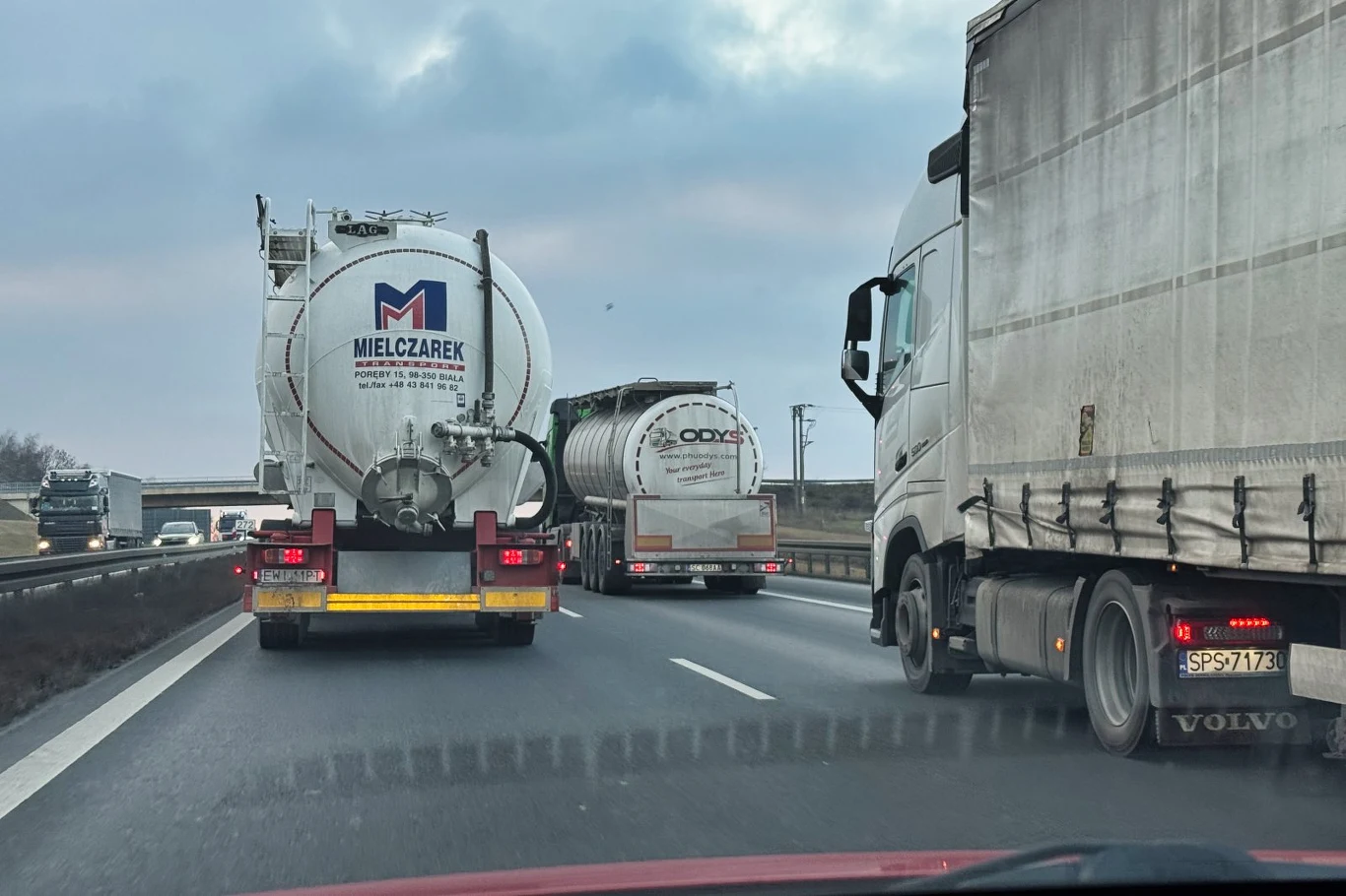 trzy duże ciężarówki jadące równolegle autostradą, z czego dwie to cysterny z widocznymi logotypami, a trzecia to samochód ciężarowy marki Volvo z plandeką
