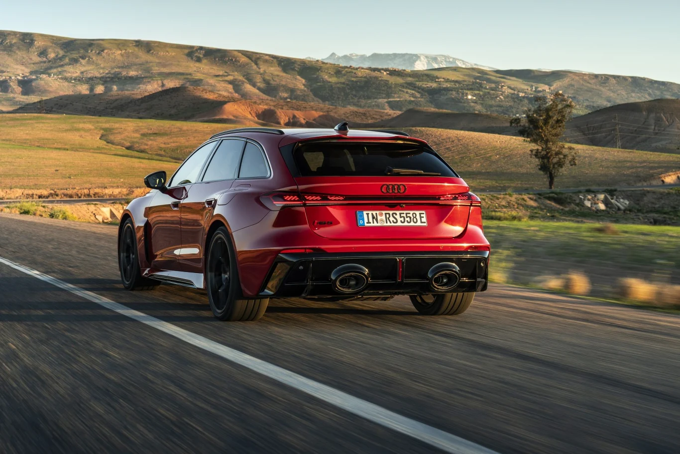 czerwone Audi RS6 Avant jadące szybką drogą przez pustynny krajobraz, wyróżniające się sportową sylwetką, dużymi felgami i czterema końcówkami wydechu