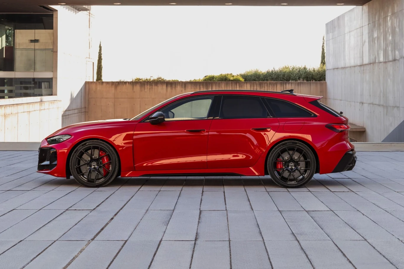 czerwone sportowe kombi z dużymi czarnymi felgami, agresywnymi liniami nadwozia i przyciemnianymi szybami ustawione profilem w nowoczesnej, minimalistycznej przestrzeni architektonicznej